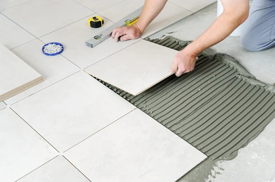 Artisan carreleur installant du carrelage blanc sur chape ciment