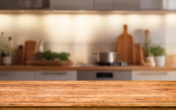 Cuisine moderne avec plan de travail en bois au premier plan, arrière-plan flou montrant des éléments culinaires et électroménager intégré