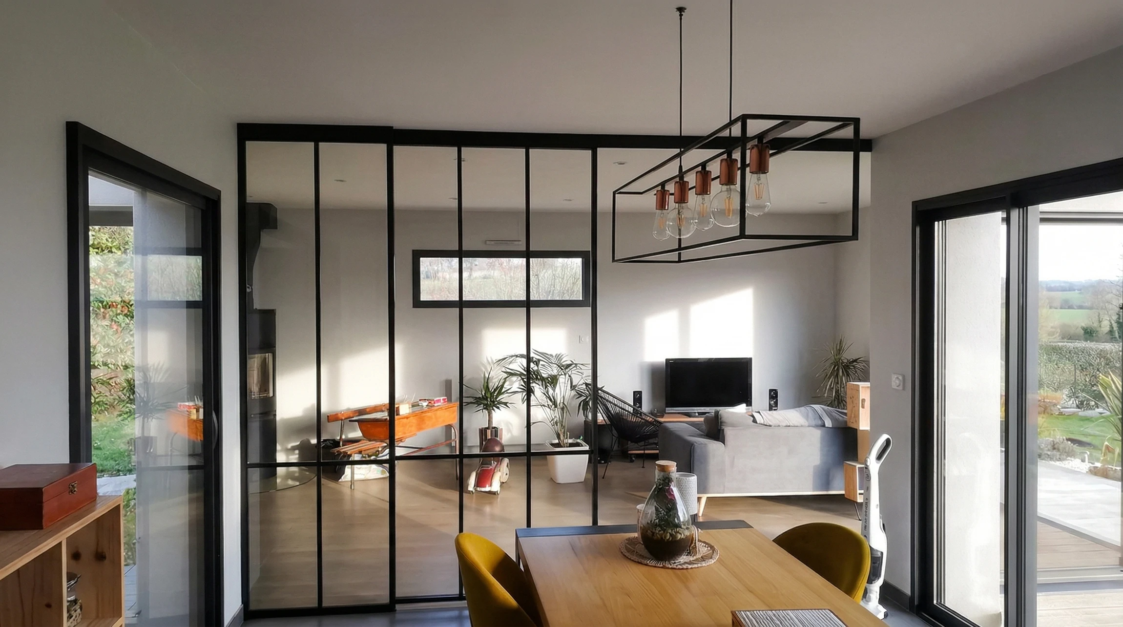 Espace de vie moderne en open space, séparé par une verrière atelier à profilés acier noirs et vitrage clair